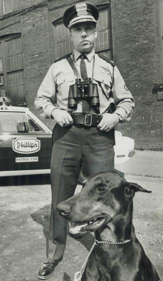 Private Cop Bruce Pickett of the Phillips Security Agency stands in front of a patrol car with Brutus, a Doberman Pinscher. His agency is one of 173 n(...)