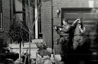 Moving in: Officers take position outside a house where two men hid following the shooting of a Peel police constable yesterday