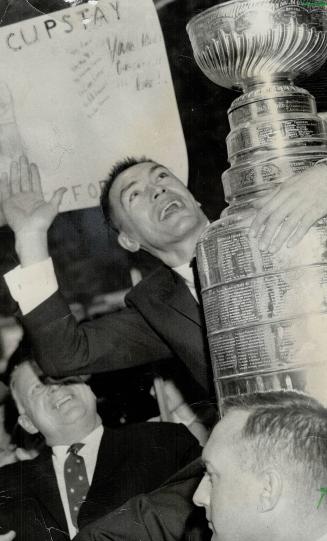 Hockey player accepts a city's gratitude as Toronto Maple Leaf team captain George Armstrong holds Stanley Cup and waves to cheering Fans in buildings(...)