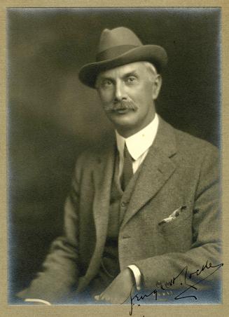 Sepia-toned studio portrait of an adult individual seated and turned slightly to the side, wear…