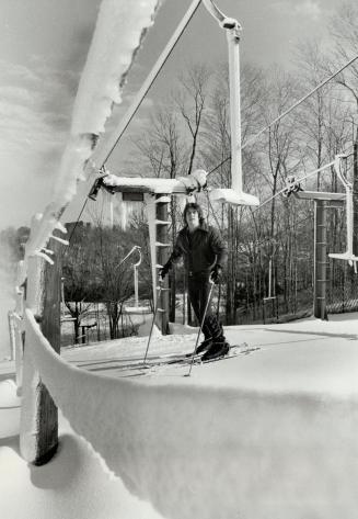 Young man on downhill skis and ski poles, standing at the top of a snowy slope.