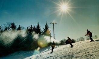 Three people skiing downhill. Photograph has lens-flare effect.