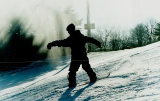 Silhouette of a person snowboarding down a hill with extended arms.