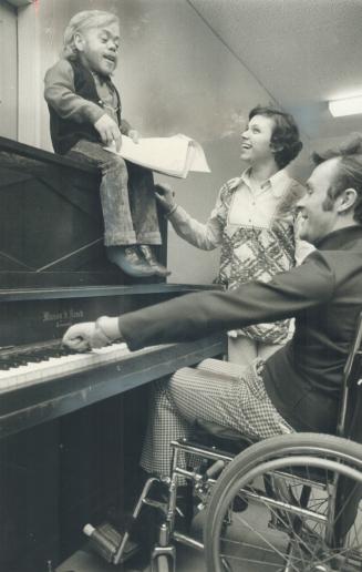 Mr. Guy Big sits on top of the piano played by Bev Hallam in St. Luke's Church, the Theatre for Physically Disabled People
