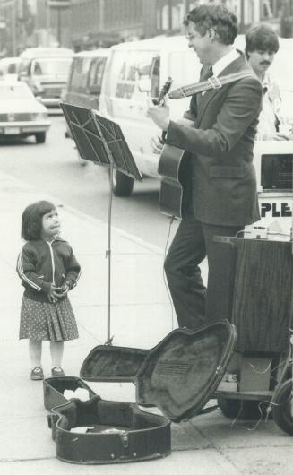 A devoted audience of one. Christine Okabe, 2, listens raptly as a musician who would give his name only as John plays classical music on his electric(...)