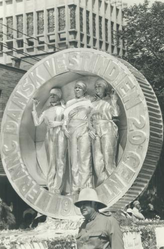 Three women in silver stand silent and motionless in a Caribbean coin on Caribana float