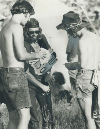 Making a buy, two youths complete a transaction with a third youth wearing a sign on his chest that advertises Acid $1
