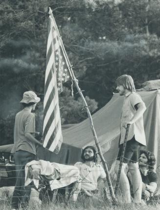 Waiting for a festival at Mosport, which may or may not get started, a group of young people stand beside their tent near a U.S. flag that is flown up(...)