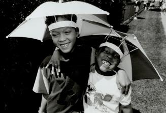 Brolly, By Golly: Louie Jacobis, 11, and his cousin Denise Hewitt, 6, who arrived at Caribana ready for either rain or sunshine, have it made in the shade with their custom all-weather headgear
