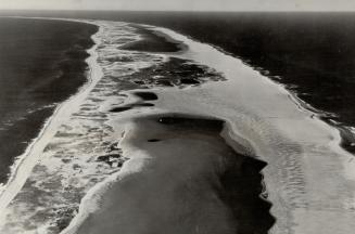 Graphically the aerial camera shows how the ever-greedy sea gnaws from all sides at this crescent-shaped sand pit