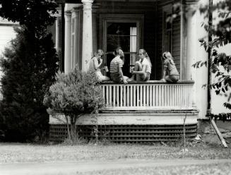 At right four girls pass the time swapping stories on the front porch