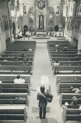 Overhead view of man with guitar standing in chapel aisle facing pulpit between two rows of spa ...