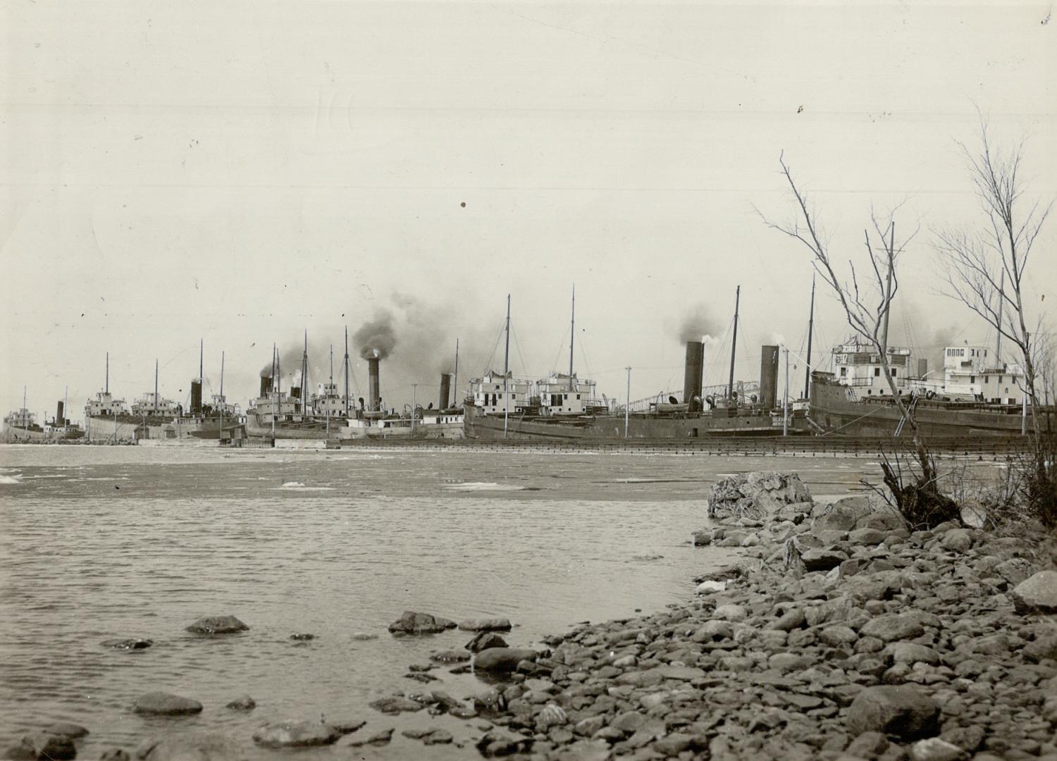 Taken from the shore, this picture shows a number of industrial buildings with many smokestacks…