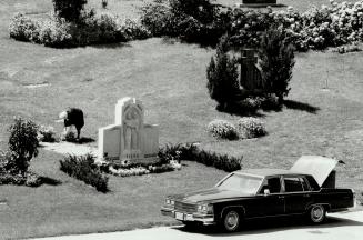 Image shows a car parked on the road by the tombstone.