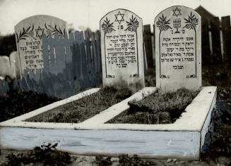 Two gravestones engraved with Hebrew text stand inside the foundation of a sarcophagus.