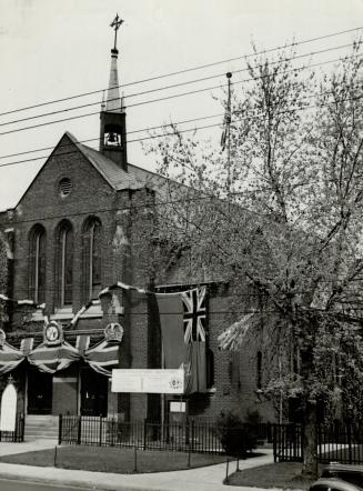 Exterior of brick church with Union Jack flags draped above entrance and replica crown affixed, ...