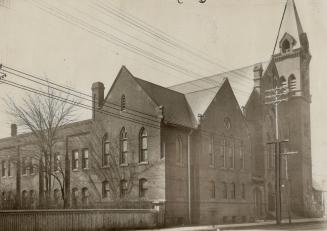 Side view of exterior of brick church with lancet windows, gable roof and attached belfry tower…