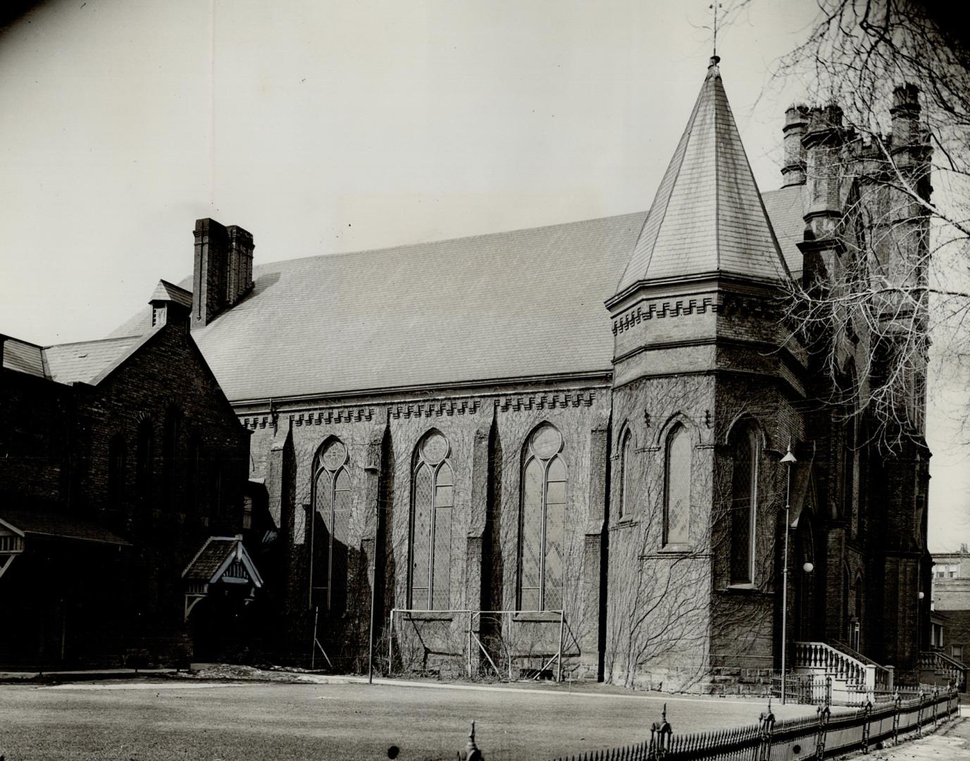 Side view of exterior of church showing arched windows, steeply pitched roof and attached tower…