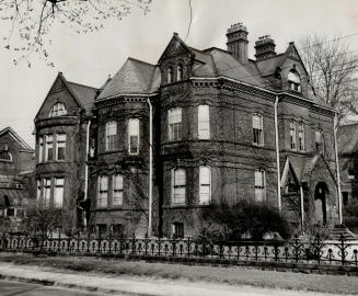 Exterior view of three-storey brick structure with dormer windows and cornice trim.