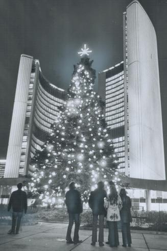 City 'Lights Up' for Christmas, Passerby pause last night, after a brief lighting-up ceremony in front of City Hall, to gaze at the lights sparkling on a giant spruce tree