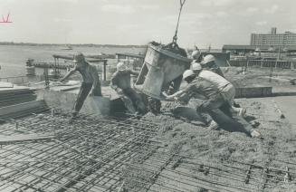 A giant ladle of cement is guided into position to be poured by workmen building the new Toronto ferry docks that will replace present dock facilities(...)