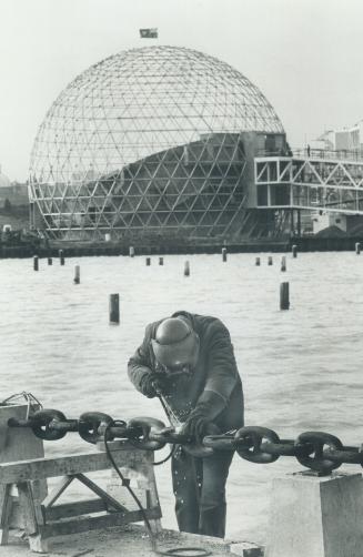 Decorative guardrail is welded from the anchor chain of two ships sunk off Exhibition Park to form a breakwater, first step in building Ontario Place.(...)