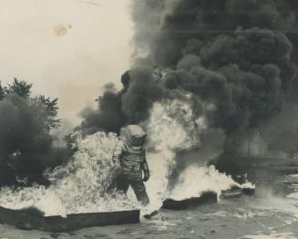 Suited for his work, Wearing an asbestos safety suit complete with its own supply of air, Alan Larimer safely walks through the flames of an oil fire (...)