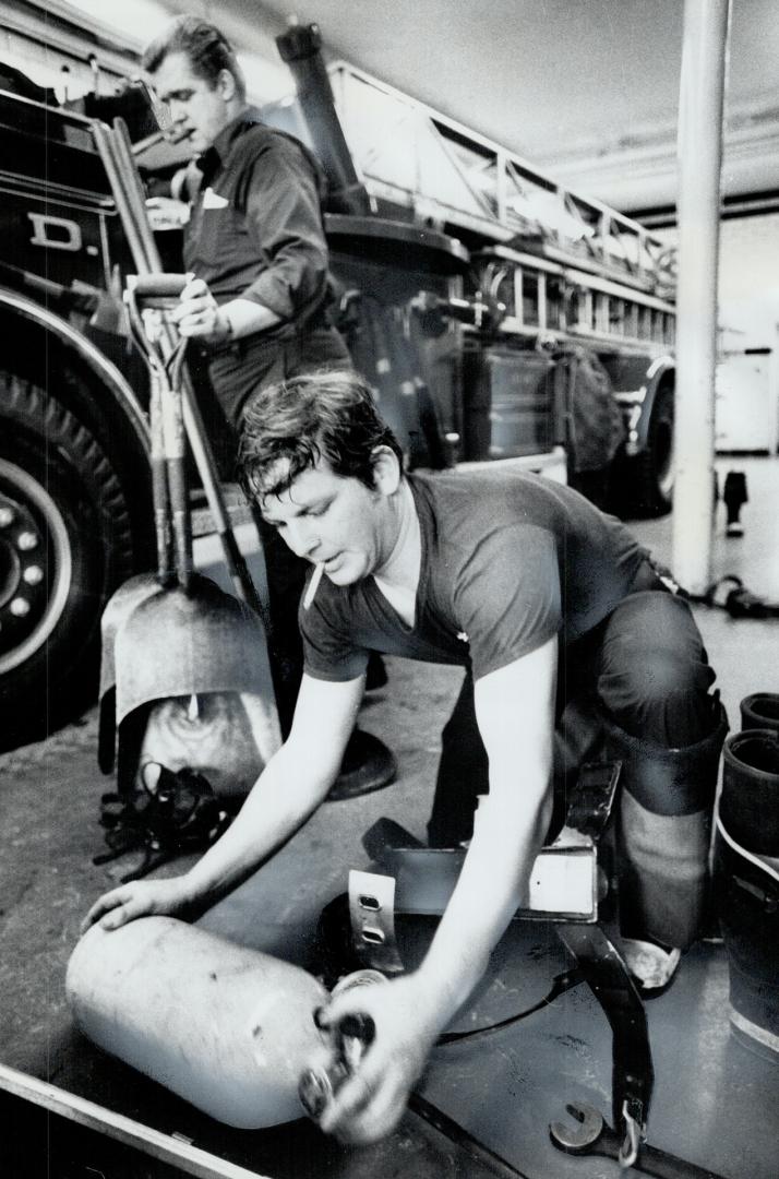 After the run to a fire, Mike O'Leary, rear, and Tim Randall clean equipment from the aerial truck and replace oxygen cylinders. This year marks the Toronto Fire Department's 100th anniversary