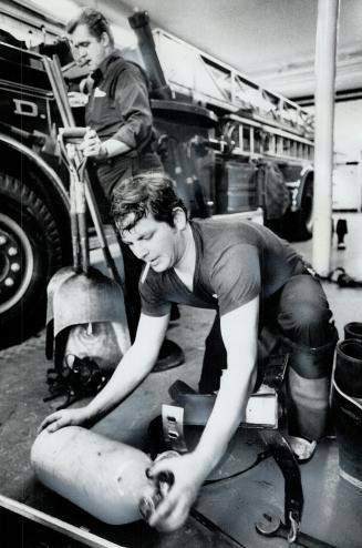 After the run to a fire, Mike O'Leary, rear, and Tim Randall clean equipment from the aerial truck and replace oxygen cylinders. This year marks the Toronto Fire Department's 100th anniversary