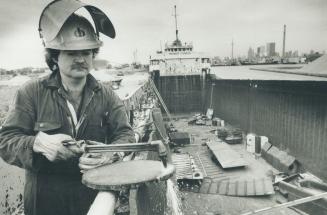 Image shows a workman with some tools in his hands at the Harbour.