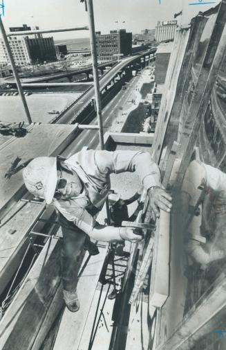 Image shows a worker with a hammer high above installing roof panes.