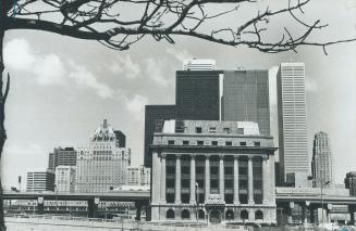 Image shows a Harbour Commission building with some skyscrapers behind it.