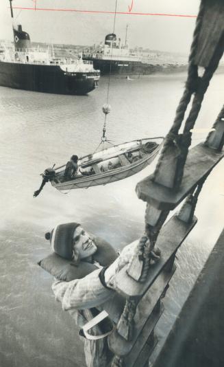 Image shows a lifeboat drill in progress: a person climbing the ladder and lifeboat being unloa ...