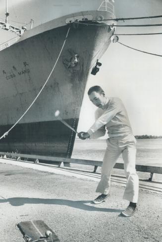 Image shows a man pretends playing golf with the cargo ship in the background.