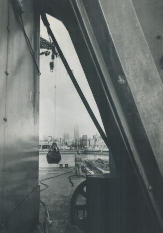 Image shows a view through a narrow gap where a construction worker looks at a crane.
