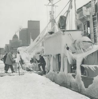 Image shows a ship at the Harbour covered with ice and snow with a few people around.