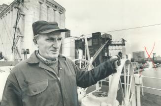 Image shows a Captain at the Harbour with some buildings and ships in the background.
