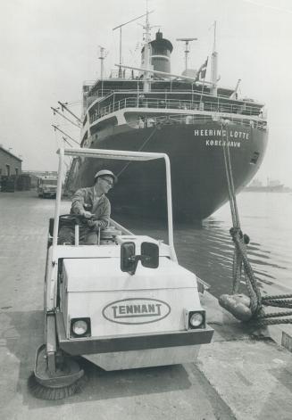 Image shows an employee in a work car in the Harbour with a big ship docked in the background.