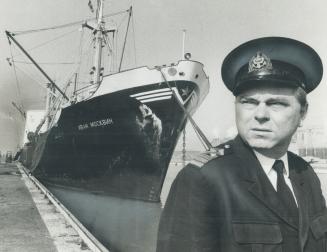 Image shows a Captain at the Harbour with the big ship in the background.