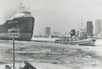 Image shows a tugboat in front of a big ship on the lake in winter.