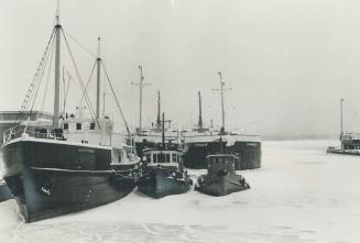 Image shows a number of bigger and smaller boats on the frozen and snow covered lake.