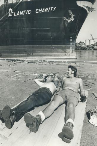Image shows two workers resting at the Harbour with the ship "Atlantic Charity" in the backgrou ...