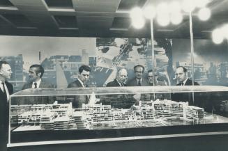 Image shows a group of people standing in front of the Harbour model under the glass.