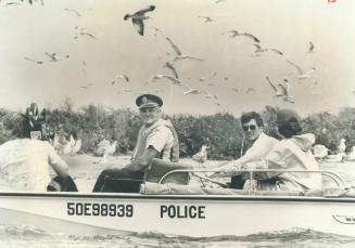 Image shows a police boat and a few people in it with a lot of sea gulls above them.