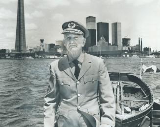 Image shows a gentleman in uniform standing by the lake with the waterfront buildings in the ba ...