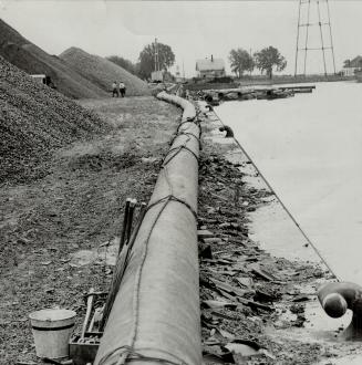 Image shows a long pipe on the ground going along the water.