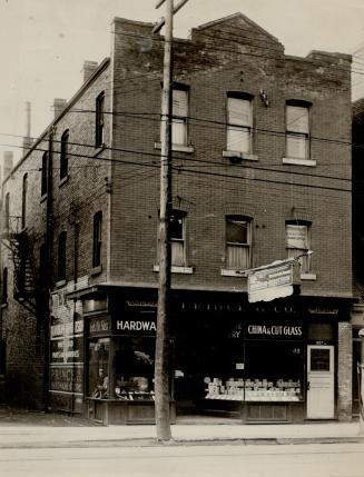 Three-storey brick building with merchandise displayed in shop windows. Signs above left and ri ...