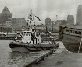 Image shows a tugboat with the Harbour buildings in the background.