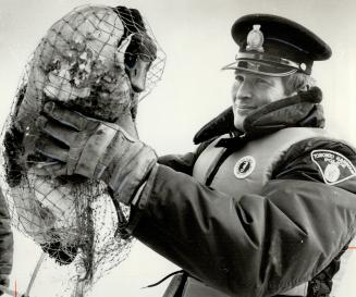 Image shows a police officer holding a goose caught in a net.