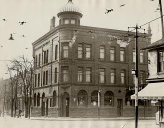 Three-storey brick building with turret at corner of intersection.